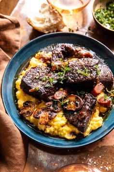 a blue plate topped with meat and grits covered in sauce next to other dishes