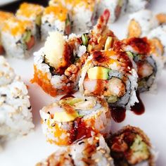 several sushi rolls are arranged on a white platter with sauce and toppings