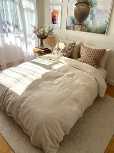 a bed with white sheets and pillows in a bedroom next to a painting on the wall