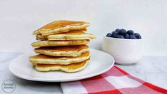 a stack of pancakes with blueberries on a plate next to a bowl of berries