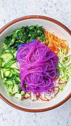 a white bowl filled with different types of veggies and noodles on top of a marble counter