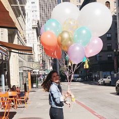 a woman is walking down the street with balloons