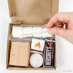 a person is holding marshmallows in a box with other items inside it