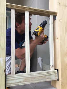 a man in blue shirt holding a drill and nailing the side of a building