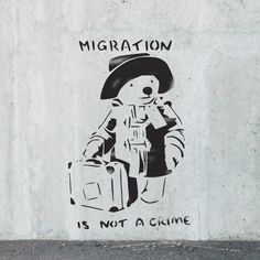 a graffiti on the side of a wall with a bear holding luggage and wearing a hat