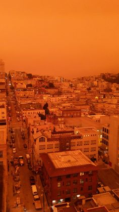 an orange sky over a city filled with tall buildings and parked cars on the street