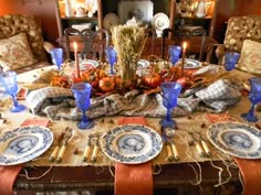 a dining room table is set with blue and white plates, silverware, pumpkins and candles