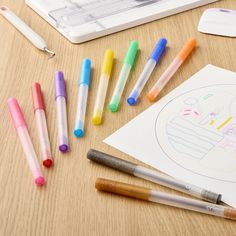 several markers and pens are sitting on a table next to a drawing pad, pencils, and paper