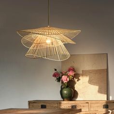 a vase with flowers sitting on top of a wooden table next to a light fixture