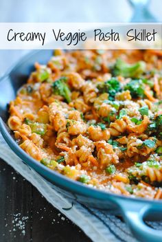 a blue pan filled with pasta and broccoli on top of a wooden table