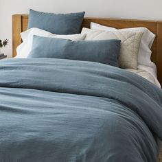 a bed with blue linens and pillows in a white walled room next to a potted plant