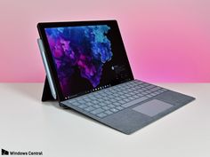 an open laptop computer sitting on top of a white table next to a pink wall