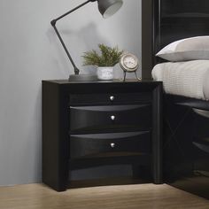 a night stand with two drawers and a clock on it, next to a bed