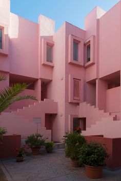 pink building with multiple balconies and plants in pots on the side walk way