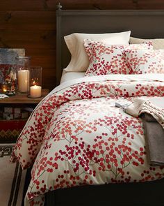 a bed with red and white comforter next to a night stand filled with candles