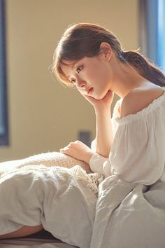 a woman sitting on top of a bed next to a window in a white dress