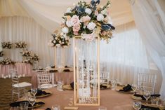 a tall vase filled with flowers sitting on top of a table covered in white linens