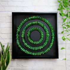 a black frame with green spirals on it next to a potted plant and white brick wall