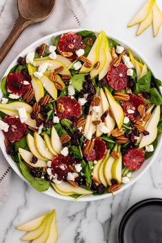 a white bowl filled with spinach, apples and cranberries on top of a marble counter