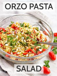 a glass bowl filled with pasta salad next to tomatoes and parsley on the side