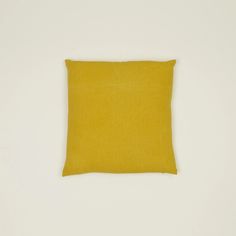 a yellow square pillow sitting on top of a white wall