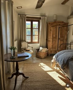 a bedroom with a bed, chair and table in it's center area next to a window