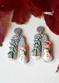 two snowman shaped earrings sitting on top of a white table next to red leaves