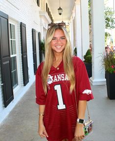 a woman in a football jersey is standing on the sidewalk with her hand in her pocket