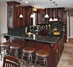 a kitchen with dark wood cabinets and granite counter tops, an island in the middle