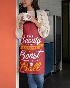 a woman is holding a coffee mug while standing next to a wall with an apron on it