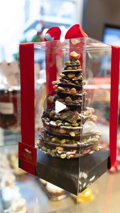 a christmas tree made out of rocks in a clear box with red ribbon around it