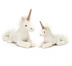 two white stuffed unicorns sitting next to each other on a white surface with one laying down