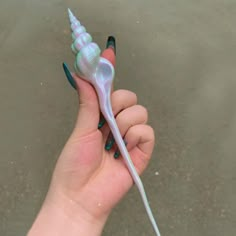 a hand holding a small white and green toy animal with long tail, on the beach