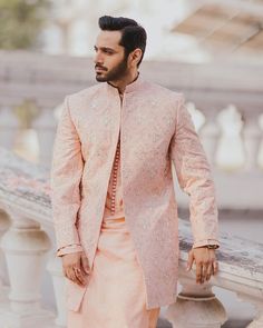 a man in a pink sherwar standing next to a white railing and looking off into the distance