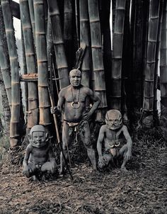 an old photo of some people in front of bamboo poles with spears and masks on