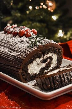 a chocolate roll with white frosting on a platter next to a christmas tree