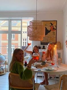 three women sitting at a table with wine glasses in front of them and one woman raising her hand