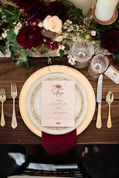 the table is set with white and gold plates, silverware, and red napkins