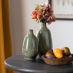 two green vases sitting on top of a wooden table next to fruit and flowers