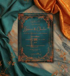 the wedding card is on top of an orange and blue cloth with gold trimmings