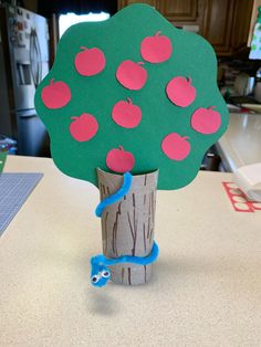 a paper tree with red apples on it and a blue snake in the middle, sitting on top of a table