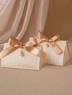 two white boxes with gold bows and pearls on them are sitting next to each other