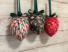 three origami pineapples hanging from hooks on a wooden wall with green ribbon