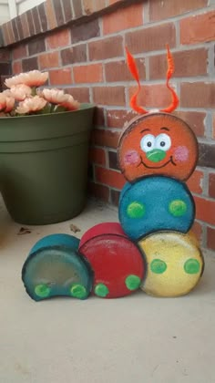 a stack of colorful rocks sitting in front of a brick wall next to a potted plant