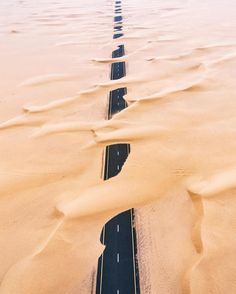 an aerial view of a road in the middle of sand dunes, with two cars driving on it