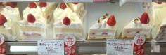 there are many pieces of cake on display in the store window, including strawberries