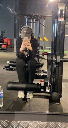 a woman sitting on top of a machine with headphones in her ears and looking at her cell phone