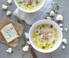 two bowls filled with soup next to some crackers and cheese on a tablecloth