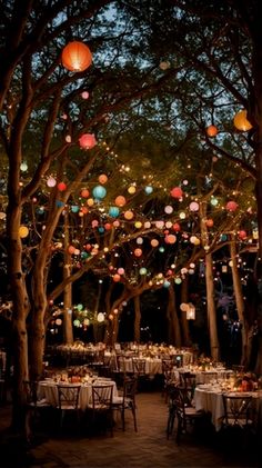 an outdoor dining area with paper lanterns hanging from the trees and tables set for dinner