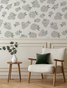 two chairs and a vase with flowers on them in front of a wallpapered background